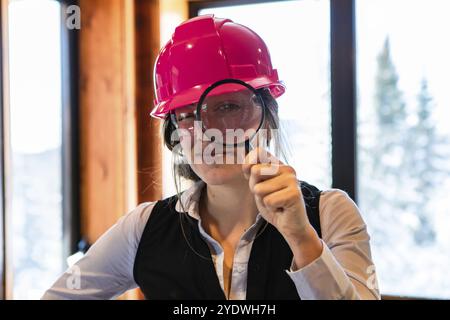 Occhio ingrandito dell'ispettore edile donna che guarda attraverso una lente d'ingrandimento. indossava un elmetto rosa durante l'ispezione della qualità dell'aria domestica Foto Stock