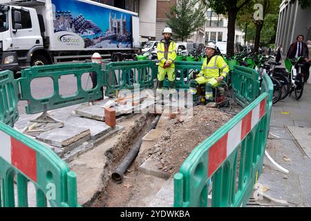 Operai del settore dei servizi pubblici operai operai che lavorano, barriere e tubi di servizi pubblici neri che scavano marciapiedi nella City di Londra Inghilterra Regno Unito KATHY DEWITT Foto Stock