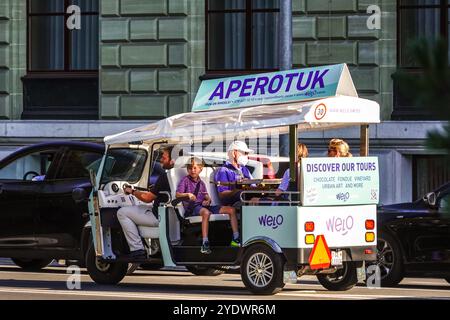 Un tuk-tuk turistico elettrico porta un gruppo di persone a visitare Quai Gustave-Ador a Ginevra, Svizzera. Foto Stock