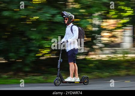 Un uomo guida il suo scooter elettrico lungo una pista ciclabile attraverso il Jardin Eglise di Ginevra, in Svizzera. Foto Stock