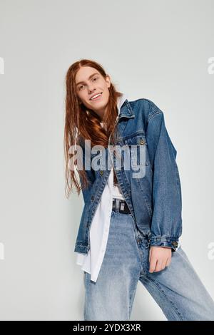 Un ragazzo adolescente mette in mostra i suoi lunghi capelli rossi e lo stile denim mentre posa in un ambiente da studio contemporaneo. Foto Stock