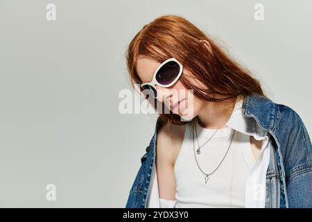 Un ragazzo adolescente mostra i suoi lunghi capelli rossi mentre posa con sicurezza in un abito in denim. Foto Stock