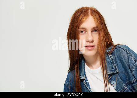 Un ragazzo adolescente mostra i suoi esclusivi capelli rossi lunghi mentre indossa un outfit di tendenza in denim in uno studio. Foto Stock