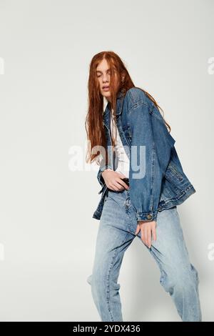 Un adolescente dai lunghi capelli rossi, sfoggia un outfit in denim in un elegante ambiente da studio. Foto Stock