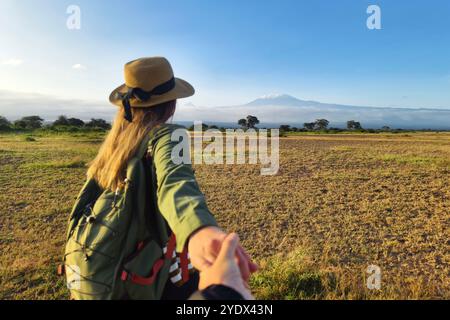 Uomo e donna camminano sullo sfondo del Kilimanjaro. Safari africano a piedi. viaggiatrice con zaino che guarda montagne incredibili, vagabondaggio Foto Stock