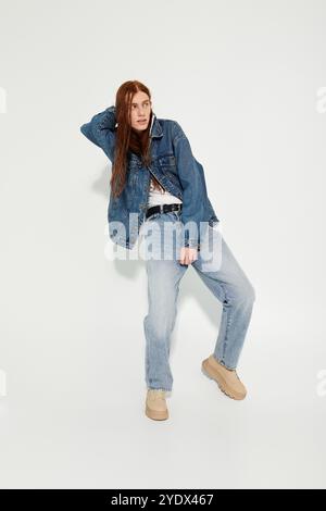 Un adolescente dai lunghi capelli rossi, sfoggia un look denim alla moda in un ambiente da studio. Foto Stock