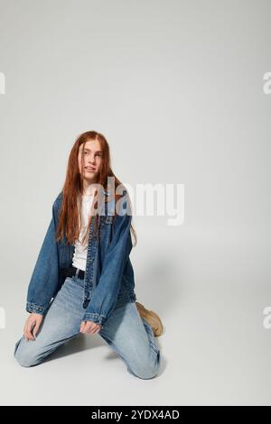 Un adolescente dai lunghi capelli rossi, sfoggia il suo outfit in denim in un ambiente creativo da studio. Foto Stock