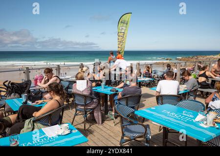 I vacanzieri si godono il sole estivo seduto sulla terrazza all'aperto del Fistral Beach Bar di Newquay in Cornovaglia nel Regno Unito. Foto Stock