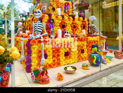 Cabina di vetro con una mostra di scheletri teschi e fiori per la celebrazione del giorno di Halloween dei morti Las Rozas Village outlet shopping Madrid Spagna Foto Stock