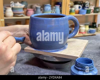 Il processo di pittura di un vaso di argilla durante una masterclass di ceramica. Artigianato e creatività in azione. Il vaso è ricoperto di smalto blu, creato Foto Stock