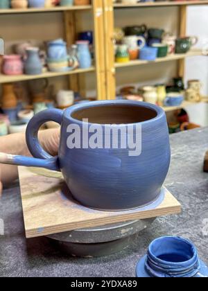 Il processo di pittura di un vaso di argilla durante una masterclass di ceramica. Artigianato e creatività in azione. Il vaso è ricoperto di smalto blu, creato Foto Stock