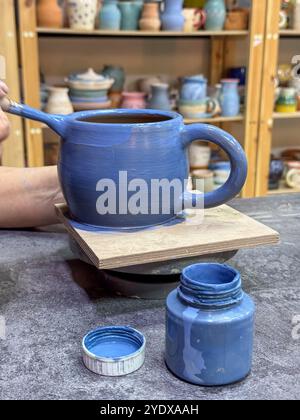 Il processo di pittura di un vaso di argilla durante una masterclass di ceramica. Artigianato e creatività in azione. Il vaso è ricoperto di smalto blu, creato Foto Stock