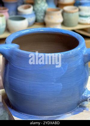 Il processo di pittura di un vaso di argilla durante una masterclass di ceramica. Artigianato e creatività in azione. Il vaso è ricoperto di smalto blu, creato Foto Stock