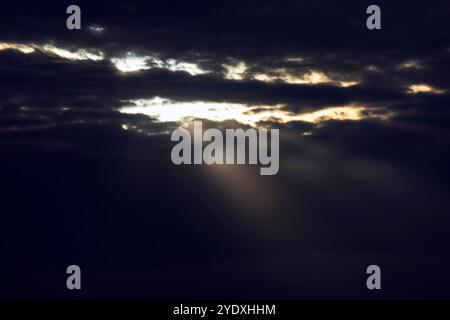 Raggi solari che si infrangono attraverso nuvole scure. Tempo tempestoso con cielo nero. Raggi luminosi che penetrano attraverso le nuvole Foto Stock