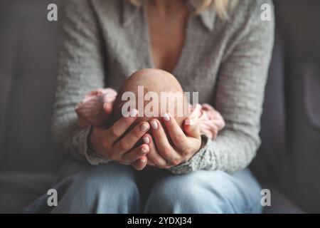Primo piano la mamma culla e dondola delicatamente il neonato tra le braccia. Concentratevi sulle mani che tengono il bambino, catturando un momento tenero e intimo di cura materna e lov Foto Stock