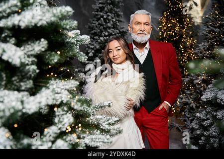 Un uomo e una donna posano insieme in abiti eleganti, circondati da scintillanti alberi di Natale. Foto Stock