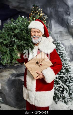 Una figura allegra racchiude un ramo di albero verde e un regalo avvolto in un ambiente ventoso. Foto Stock