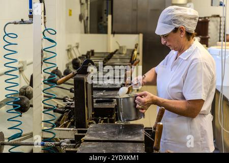 Un dipendente con abiti da lavoro bianchi e un cappuccio riempie un ferro da stiro per cialde nella fabbrica di cialde la Serenissima. Via XXV marzo, Domagnano, San Marino Foto Stock