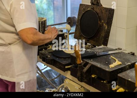 Un dipendente di la Serenissima versa la pastella su un ferro da stiro per cialde. I segni di utilizzo rivelano che si tratta ancora della prima generazione di ferri da stiro a cialda, con la quale la produzione industriale è iniziata nel 1942. Via XXV marzo, Domagnano, San Marino Foto Stock