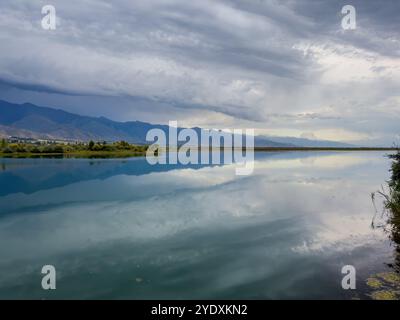 Le calme acque del lago Issyk-Kul riflettono le nuvole e le montagne spettacolari. Silenzio e tranquillità in un'oasi naturale del Kirghizistan. Foto Stock