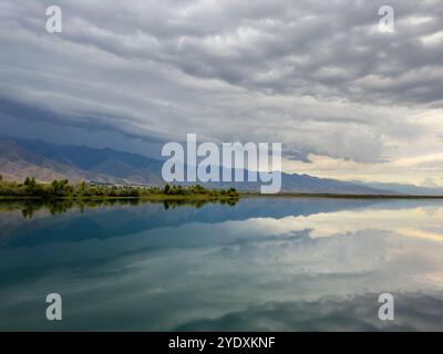 Le calme acque del lago Issyk-Kul riflettono le nuvole e le montagne spettacolari. Silenzio e tranquillità in un'oasi naturale del Kirghizistan. Foto Stock