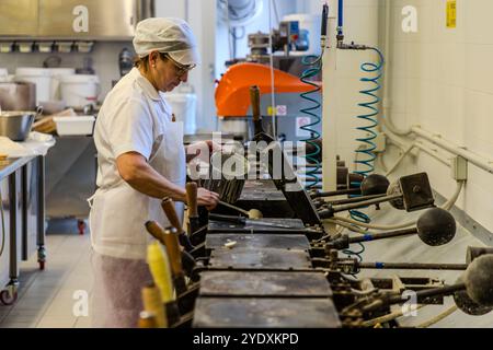 Un dipendente con abiti da lavoro bianchi e un cappuccio riempie un ferro da stiro per cialde nella fabbrica di cialde la Serenissima. Via XXV marzo, Domagnano, San Marino Foto Stock