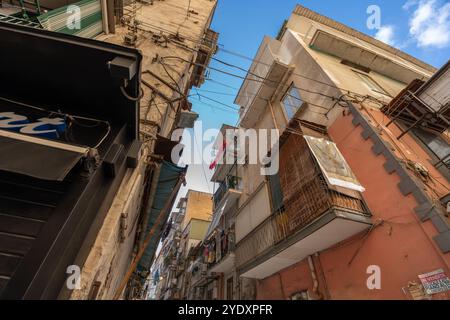 Napoli, Italia - 23 maggio 2024: Vivace vicolo urbano a Napoli, Italia, con Clothesline drappeggiate tra alti, edifici intemprati, cavi sospesi e a. Foto Stock