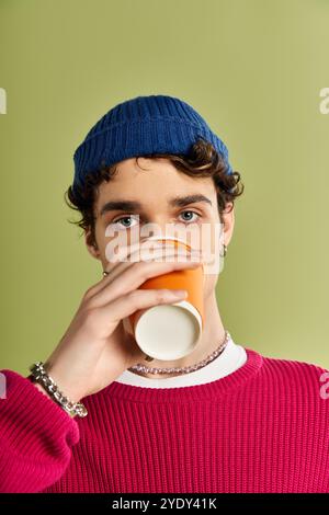 Un giovane elegante sorseggia una tazza di caffè, mostrando il suo stile unico su un morbido sfondo verde. Foto Stock