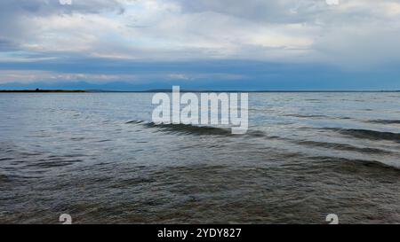 Le calme acque del lago Issyk-Kul riflettono le nuvole e le montagne spettacolari. Silenzio e tranquillità in un'oasi naturale del Kirghizistan. Foto Stock