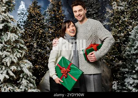 Una coppia si abbraccia con gioia tra alberi innevati, condividendo regali festivi e auguri calorosi per le vacanze. Foto Stock