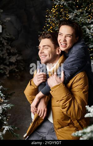 Una coppia felice in giacche accoglienti condivide un momento caldo tra pini innevati che celebrano il Natale. Foto Stock