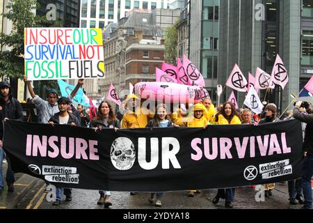 Londra, Inghilterra, Regno Unito. 28 ottobre 2024. I manifestanti marciano attraverso la città di Londra con bandiere e una barca gonfiabile, dietro uno striscione che dice "˜assicurare la nostra sopravvivenza”. Extinction Rebellion (XR) cammina per la City di Londra e fermati e dimostra fuori dagli uffici delle compagnie di assicurazione che continuano ad assicurare le compagnie di combustibili fossili nonostante gli avvertimenti di una crisi climatica da parte degli scienziati. I manifestanti credono che se le compagnie assicurative cessassero il loro coinvolgimento con queste compagnie avrebbero lottato per continuare a lavorare con le mie. L'azione è la prima di una settimana di protesta diretta spec Foto Stock