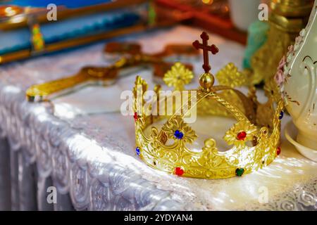 Una corona dorata adornata di gioielli poggia su un altare splendidamente disposto, illuminato da luce soffusa. Foto Stock