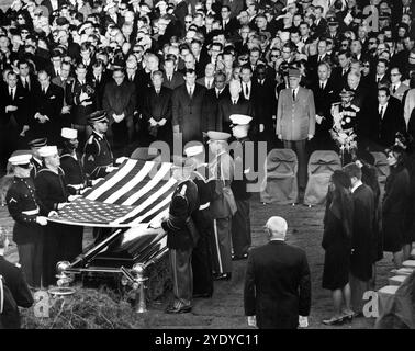 I membri della famiglia Kennedy, i funzionari e i dignitari si guardano come guardiani d'onore sollevano la bandiera del presidente degli Stati Uniti John F. Kennedy al cimitero, durante i funerali di stato del presidente Kennedy, Arlington National Cemetery, Arlington, Virginia, USA, Abbie Rowe, White House Photographs, 25 novembre 1963 Foto Stock