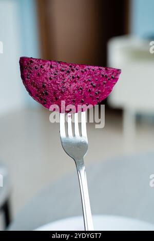 Una fetta vibrante di frutta di drago tenuta su una forchetta pronta per essere gustata. Foto Stock