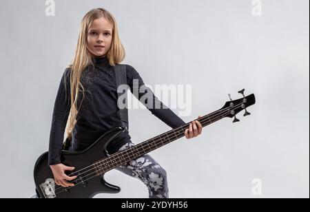 Giovane musicista sicura di sé con lunghi capelli biondi che suona con passione il basso elettrico, mostrando il suo talento musicale e il suo amore per la musica rock ag Foto Stock