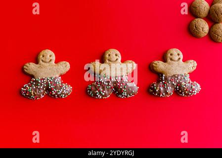 Tre uomini di pan di zenzero e piccoli biscotti speziati su sfondo rosso Foto Stock