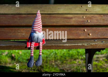 Uno gnomo natalizio seduto su una panchina di legno nel parco in una soleggiata giornata autunnale. Copia spazio Foto Stock