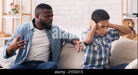 Piccolo afro ragazzo che copre le orecchie per non ascoltare arrabbiato padre scolding Foto Stock