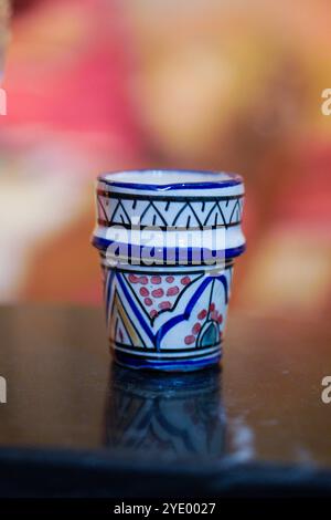 Una piccola tazza in ceramica marocchina dal design complesso con motivi colorati, tra cui forme geometriche e motivi floreali, collocata su una superficie riflettente Foto Stock