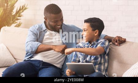 Afro padre e figlio hanno sbattere i pugni, celebrando la vittoria con il tablet digitale Foto Stock