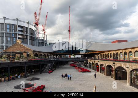 Gli amanti dello shopping camminano attraverso il Coal Drops Yard, un centro commerciale che utilizza edifici industriali riutilizzati nell'area di riqualificazione di King's Cross a Londra. Foto Stock