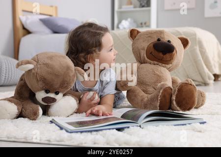 Una bambina carina che legge un libro e orsacchiotto sul pavimento di casa Foto Stock