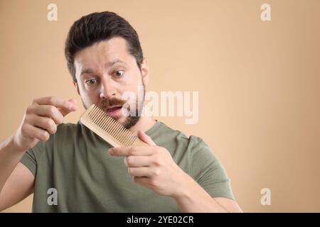 Uomo triste che prende i capelli persi dal pettine su sfondo beige, spazio per il testo. Problema di alopecia Foto Stock