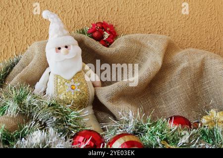 Babbo Natale in feltro imbottito con abito bianco e dorato. Decorazioni natalizie natalizie con festoni verdi e baubles di colore rosso e dorato. Foto Stock