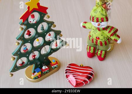 Pupazzo di neve ripieno e giocattolo per l'albero di Natale su sfondo in legno per le festività di dicembre. Baule natalizie, decorazioni per la stagione invernale, rosso e verde. Foto Stock