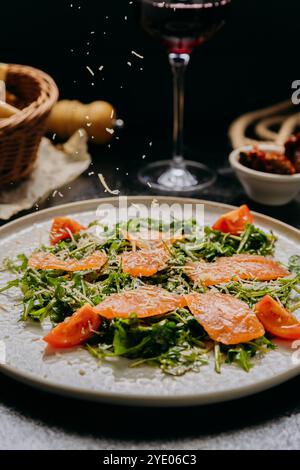 Insalata di rucola con salmone affumicato, pomodori ciliegini e parmigiano grattugiato fresco, servito con vino rosso Foto Stock