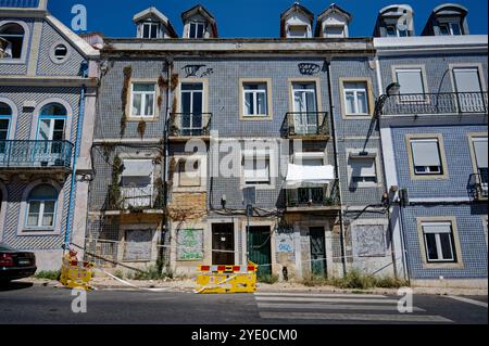 Un edificio in piastrelle condannato ad Alfama mostra segni di età e degrado urbano, con azulejos blu vibranti che contrastano con le pareti logore Foto Stock