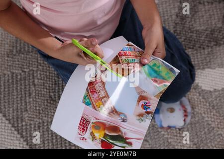 Creazione della bacheca di visione. Ragazza che taglia la foto sul pavimento in interni, vista dall'alto Foto Stock