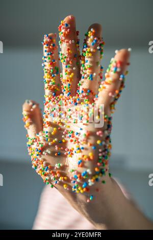 La mano della donna ricoperta di colorate cospargette di zucchero per la topping della panetteria e decorazioni colorate per la cottura. Foto Stock